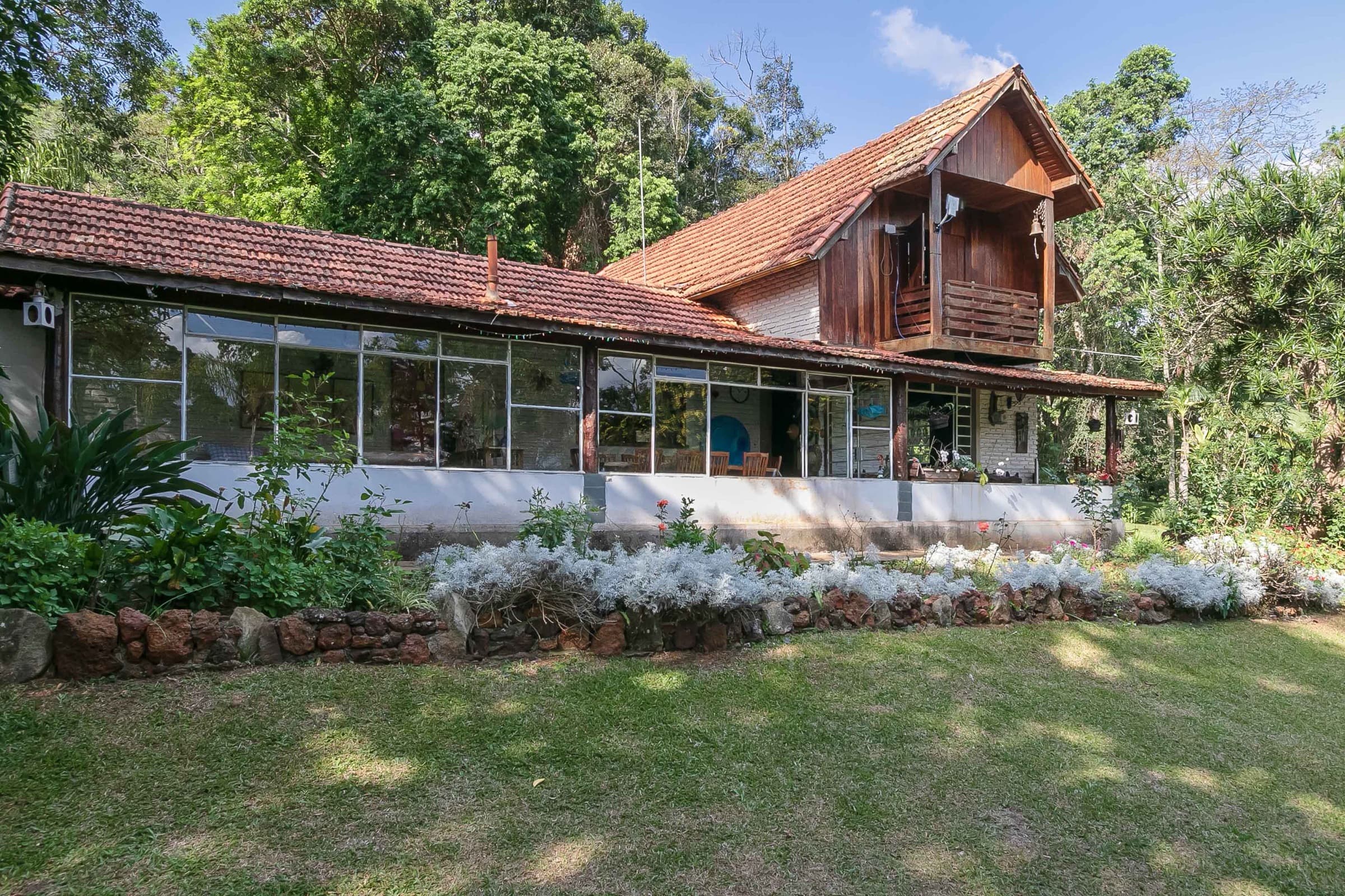 A casa principal do Chalé do Alto, com varanda envidraçada, cercada pela mata